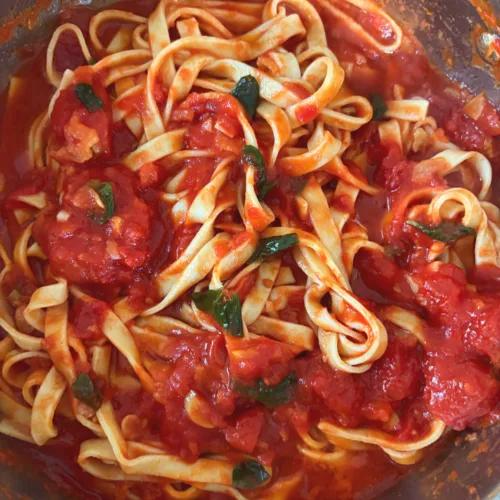 Fresh pasta tossed with a simple Italian tomato sauce and basil in a pan.