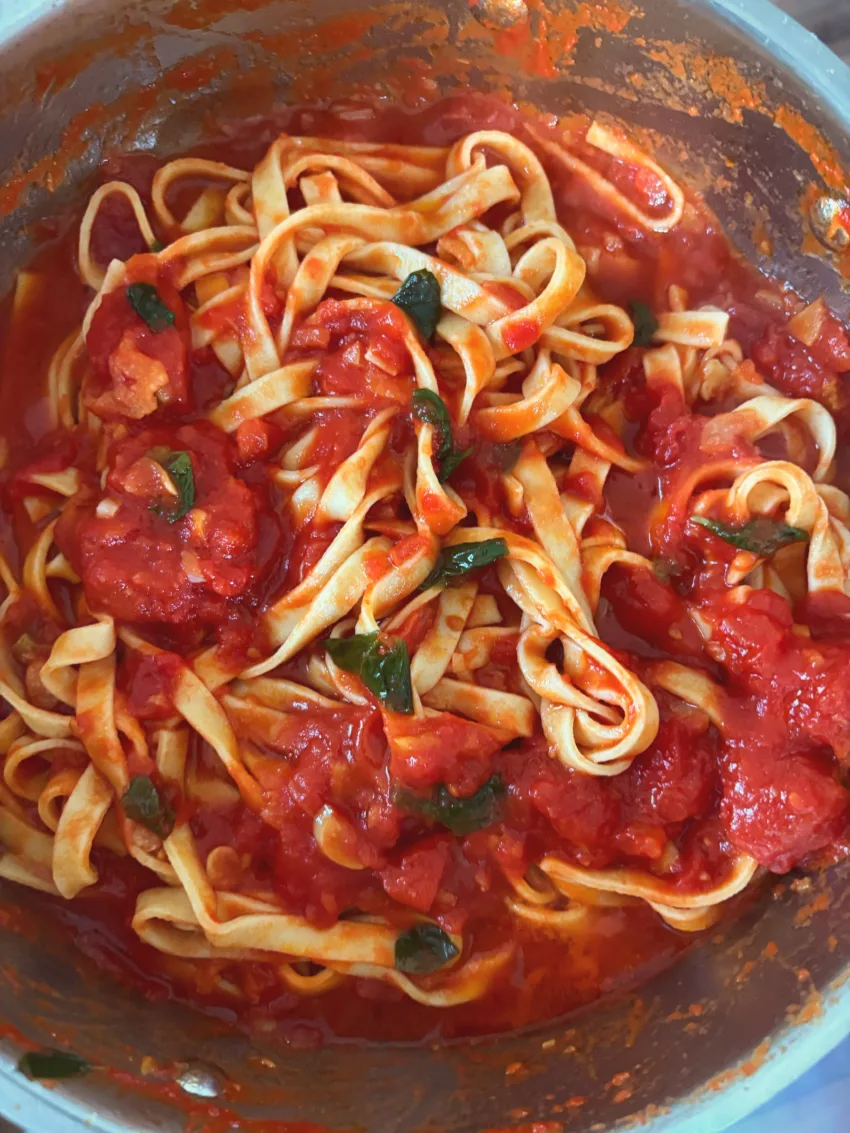 Fresh pasta tossed with a simple Italian tomato sauce and basil in a pan.