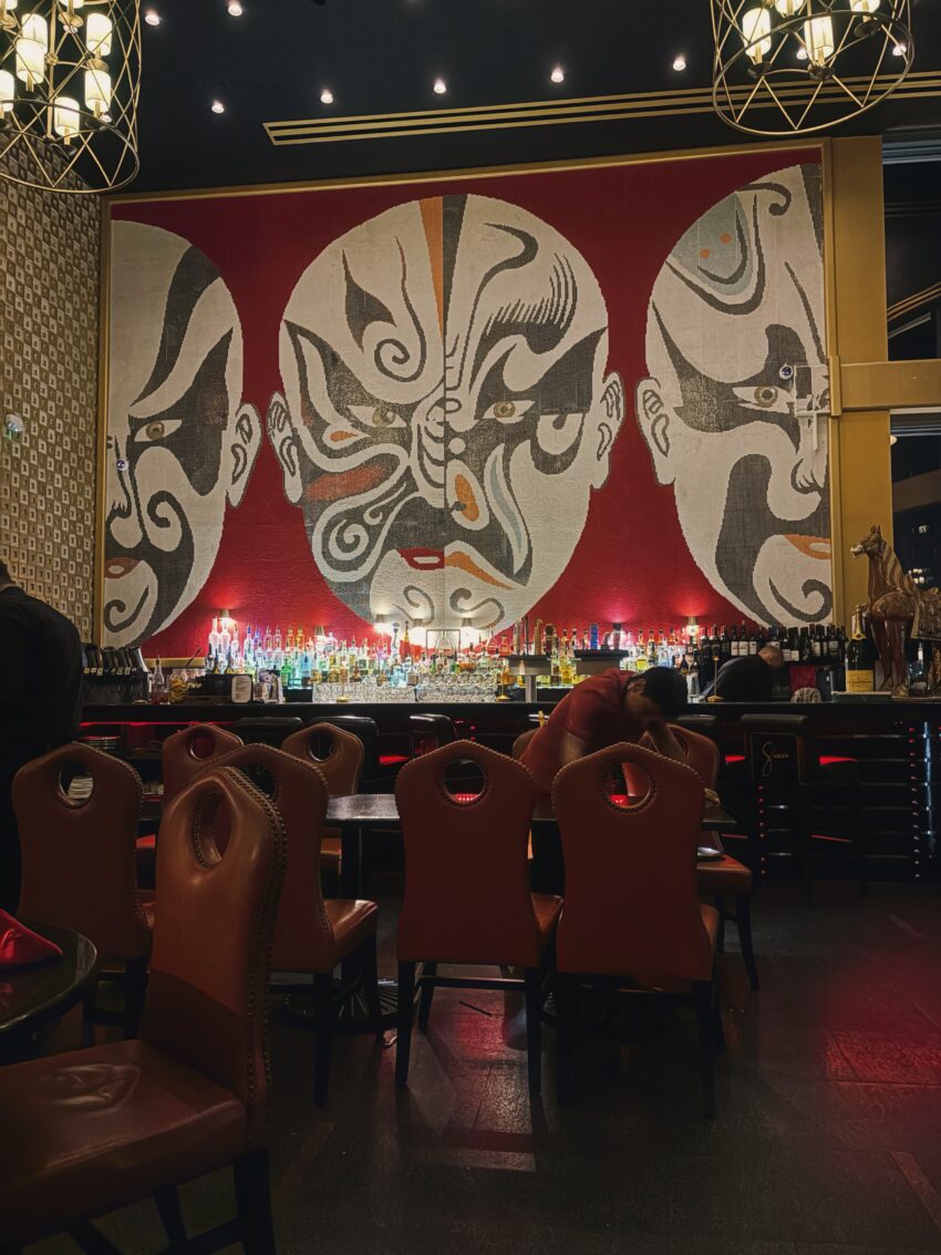 A colorful bar interior with a mural of faces and bold contrasting colors, viewed from a seated table perspective.