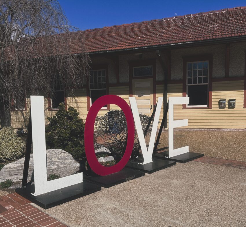 Large freestanding letters spelling the word “LOVE” displayed outdoors along a town’s Main Street.