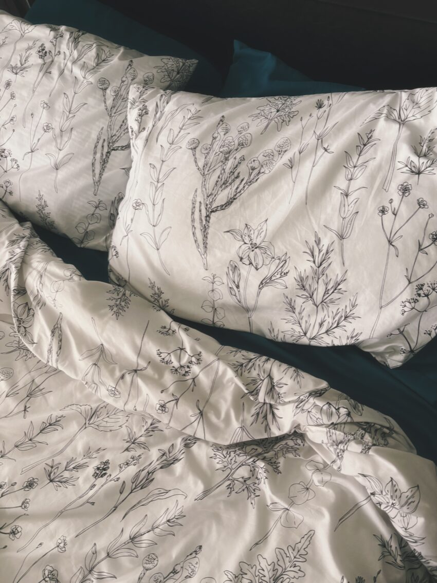 An unmade bed with neutral bedding, pillows, and a simple duvet lit by soft natural morning light.