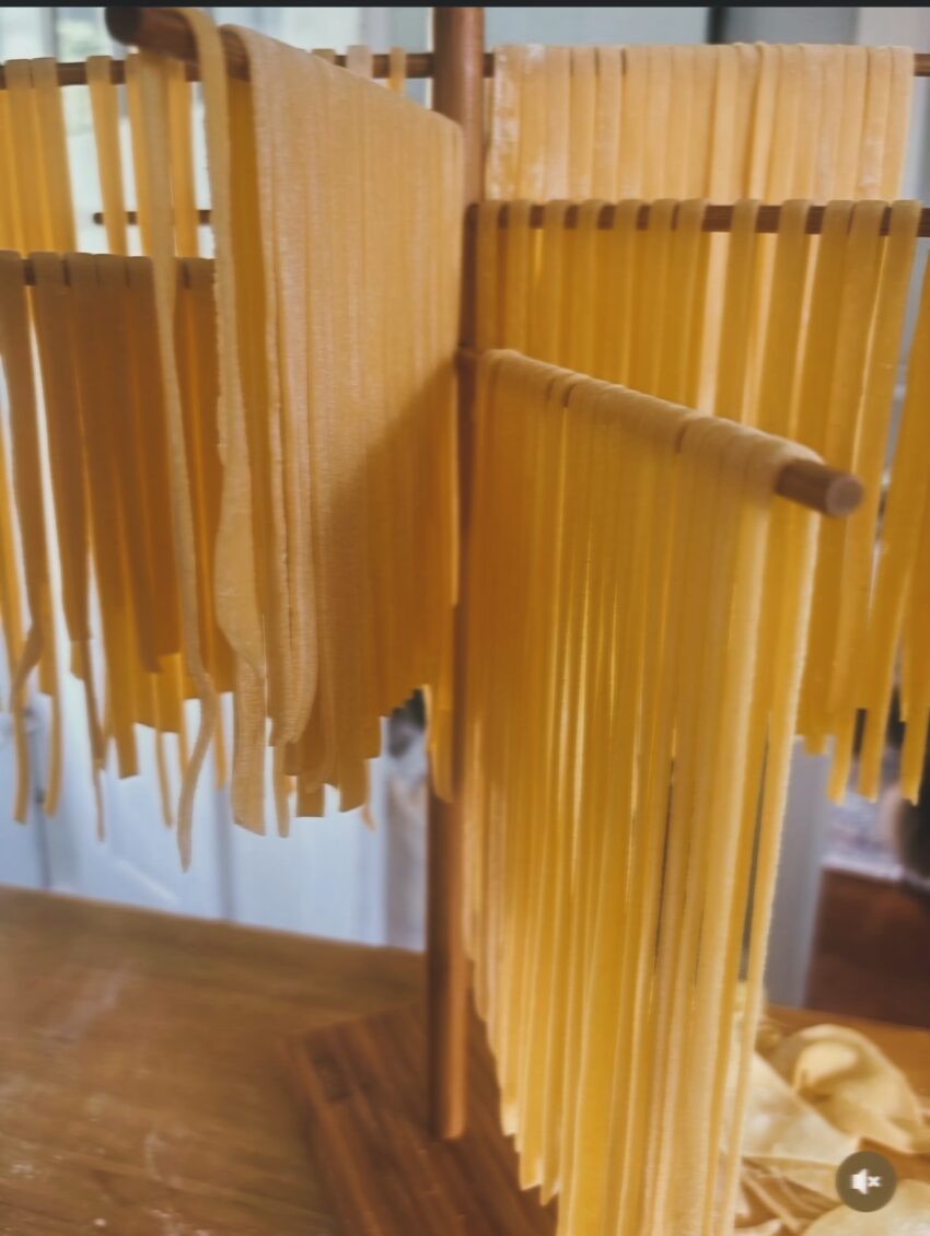 Freshly made pasta strands hanging on a pasta drying rack in a home kitchen.