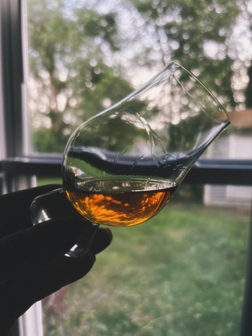 A close-up of a whiskey glass held to the light, showing the slow legs of the whiskey running down the inside of the glass.