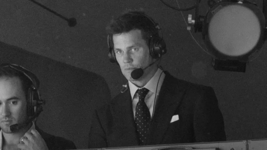 Tom Brady in the broadcast booth looking down toward the field during an NFL game
