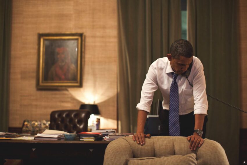 Barack Obama with sleeves rolled up, listening attentively during a phone call alone in the Oval Office.