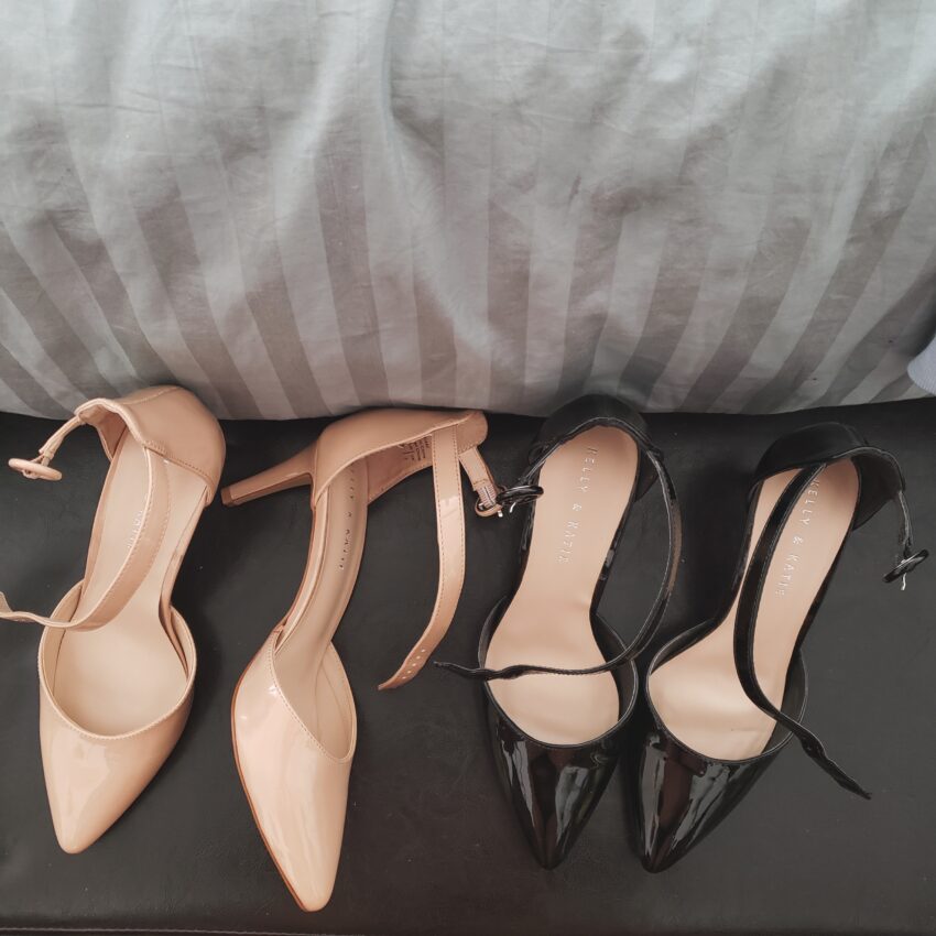 Two pairs of heels sitting on a padded bench at the foot of the bed. One nude, one black.