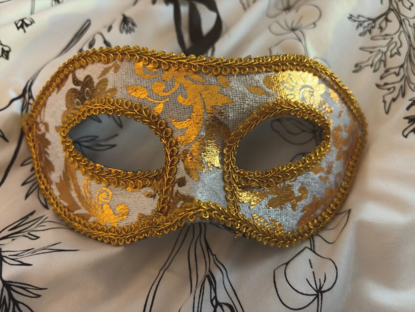A gold and white masquerade mask photographed in soft light, evoking stillness, mystery, and quiet intimacy.