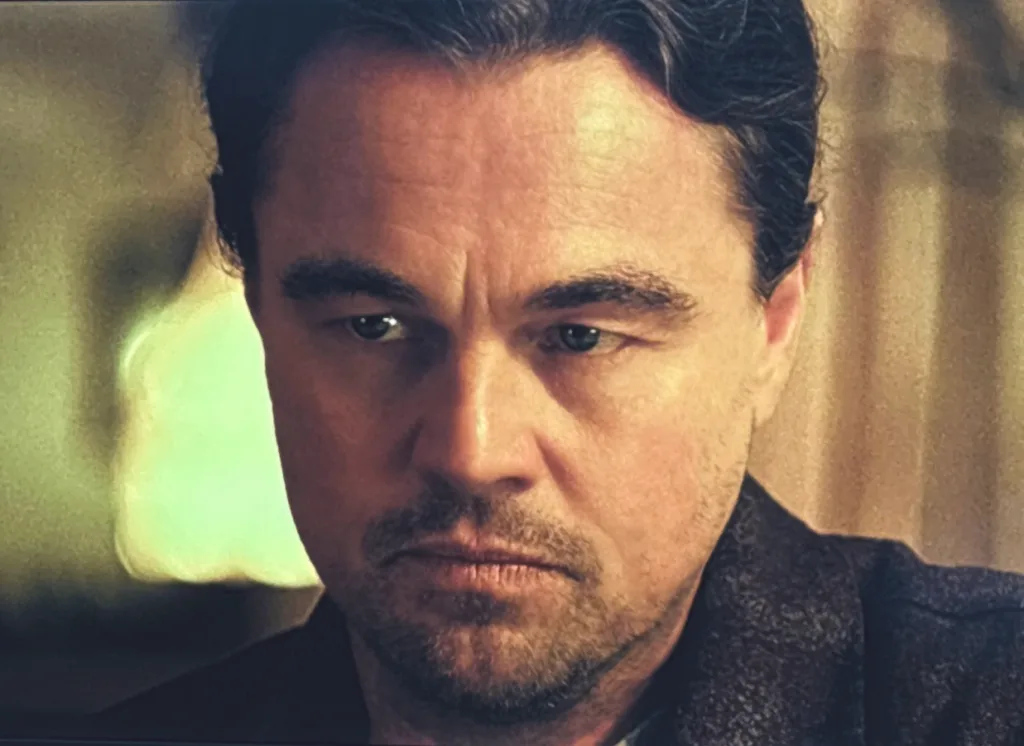 A man sits still with a serious, inward expression, listening intently during a tense conversation.