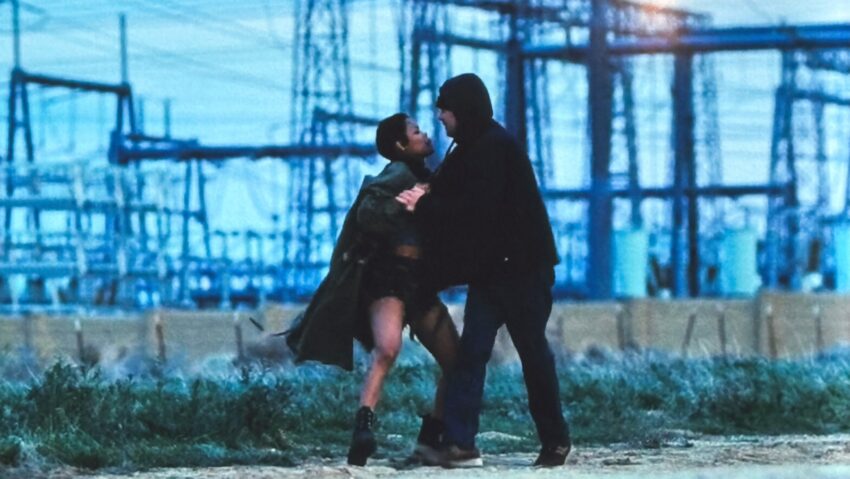 Two people run near an industrial site as one grabs the other, interrupting their movement away from a dangerous situation.