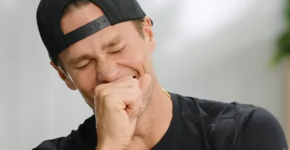 Tom Brady in casual black cap and shirt, smiling in a relaxed, genuine moment during a candid conversation.