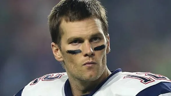 Tom Brady in NFL uniform and eye black, expression focused and serious during a game.